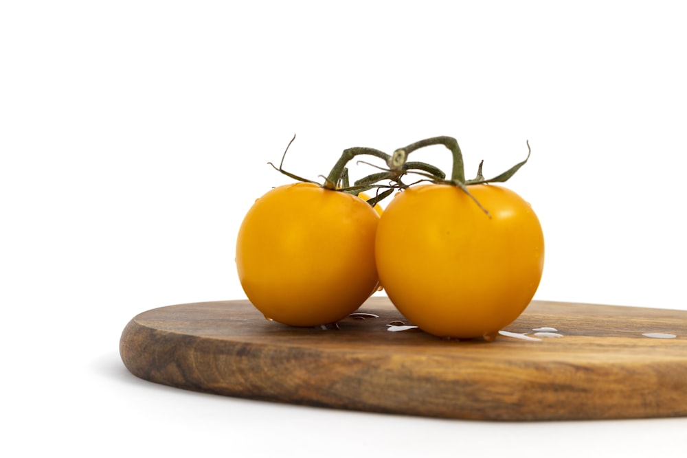 two yellow tomatoes sitting on top of a wooden cutting board