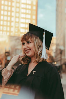 A vibrant photo of a student celebrating graduation with a city skyline glowing in the background at dusk.