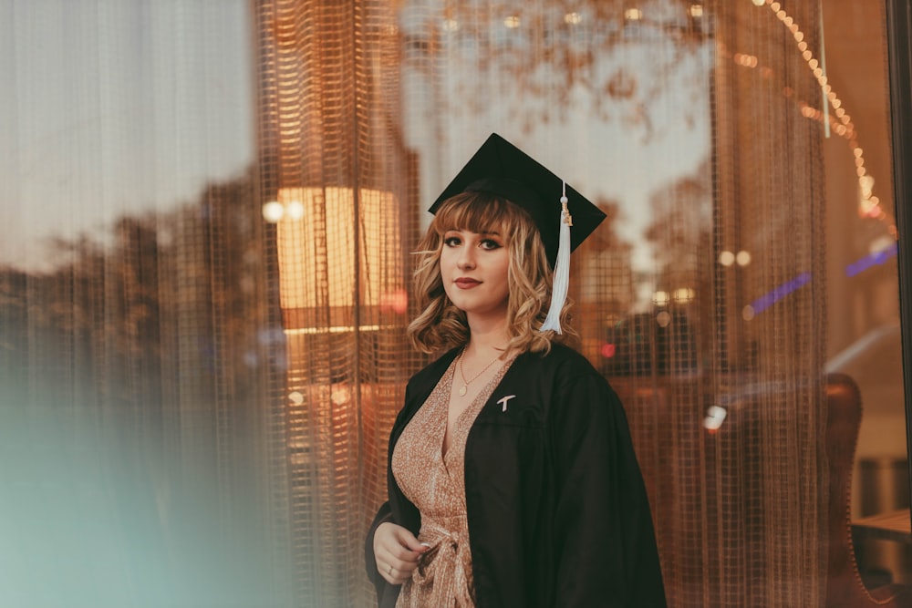 a woman in a graduation cap and gown standing in front of a window