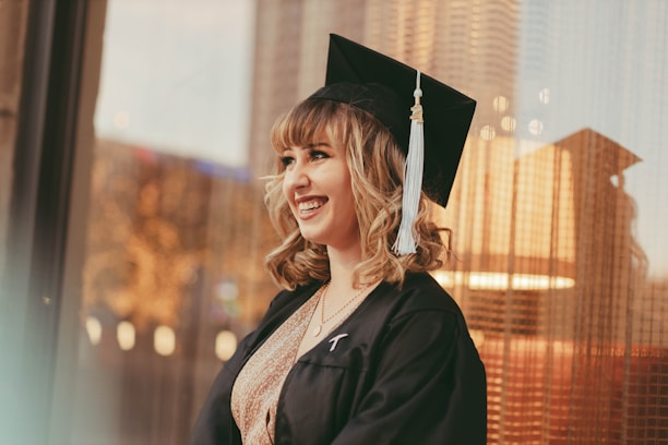 A joyful portrait of a young graduate in cap and gown, smiling genuinely against a soft, blurred background.