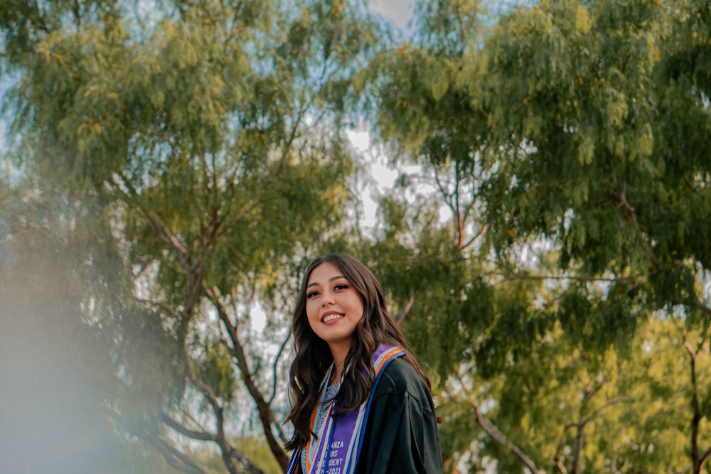 a woman in a graduation gown standing in front of trees