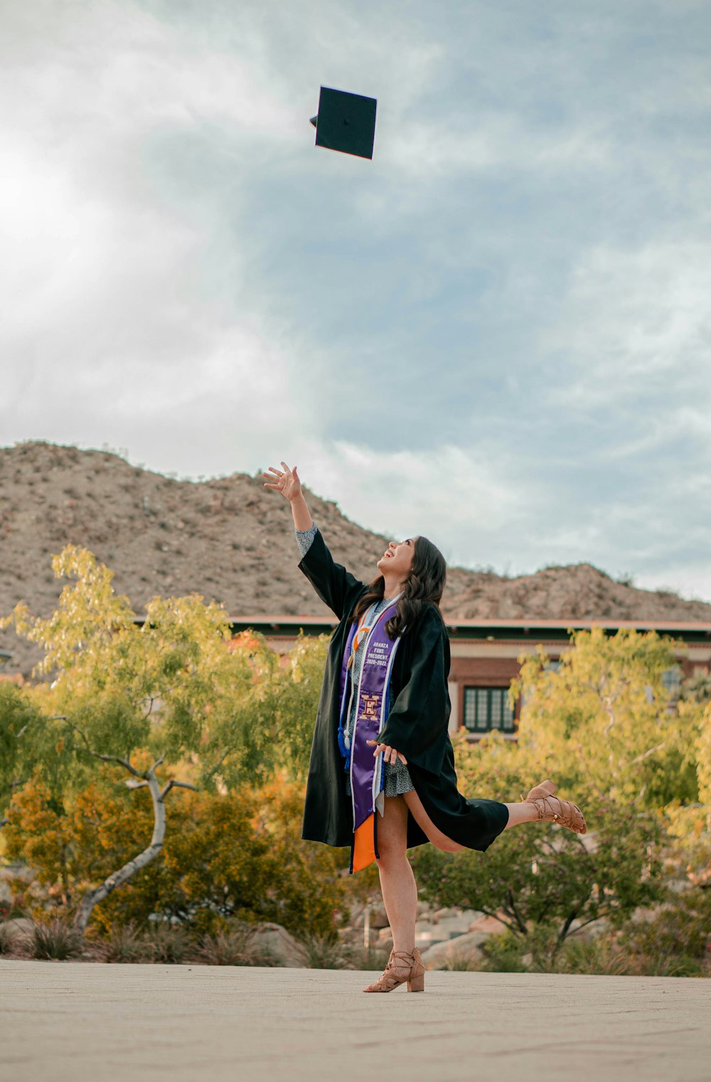 Una donna in un abito di laurea che lancia un berretto di laurea in aria