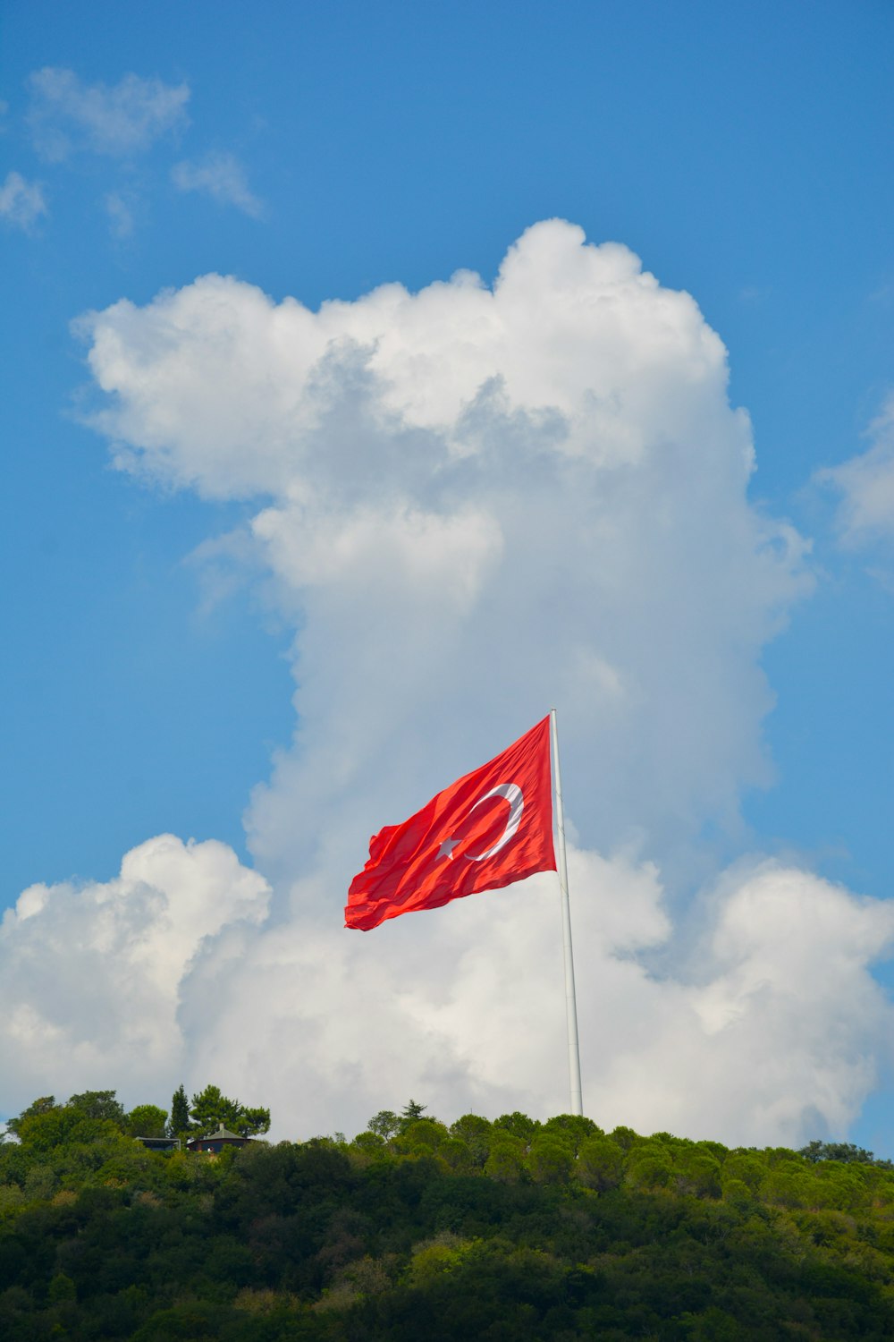 a red flag on top of a hill under a cloudy blue sky