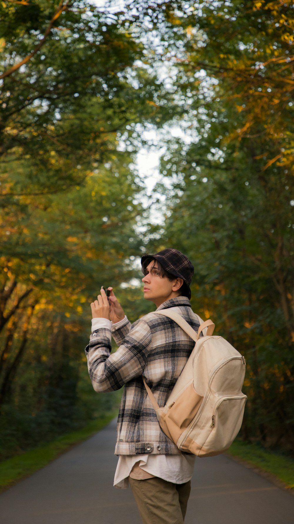 A young man standing in the middle of a forest road, admiring nature & taking photographs