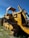 A large, yellow bulldozer with a canopy is parked on a grassy area. The machinery is detailed with metal treads and hydraulic components. A clear blue sky forms the background, while power lines run across the horizon.