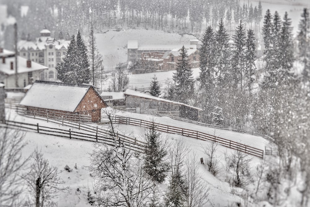 a snowy landscape with a barn and a fence in the foreground