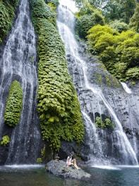 two people sitting on a rock in front of a waterfall