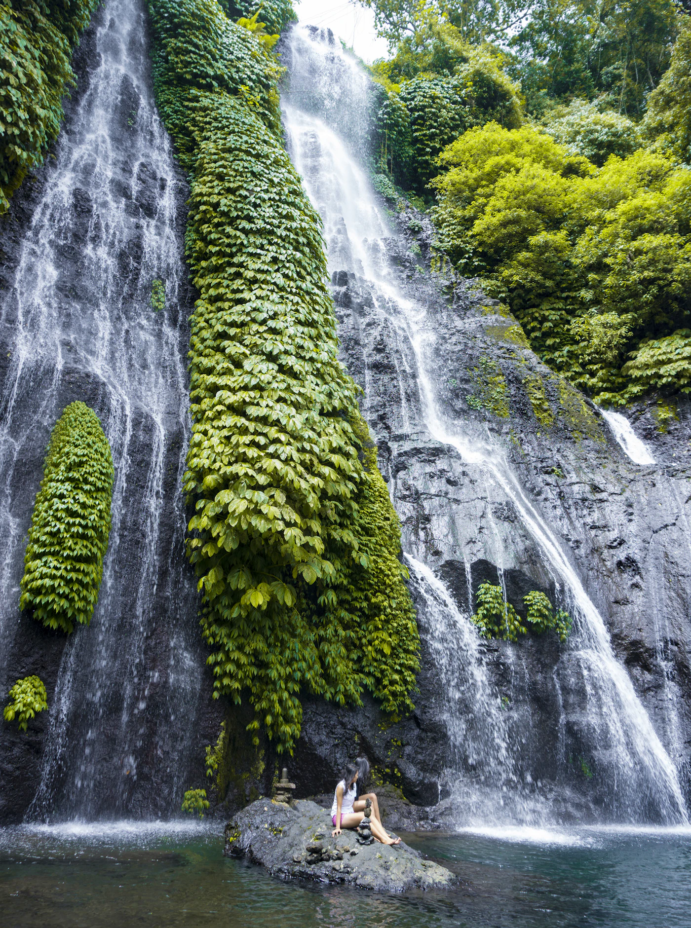 Two travellers sitting on a rock in front of Banyumala Twin Waterfall