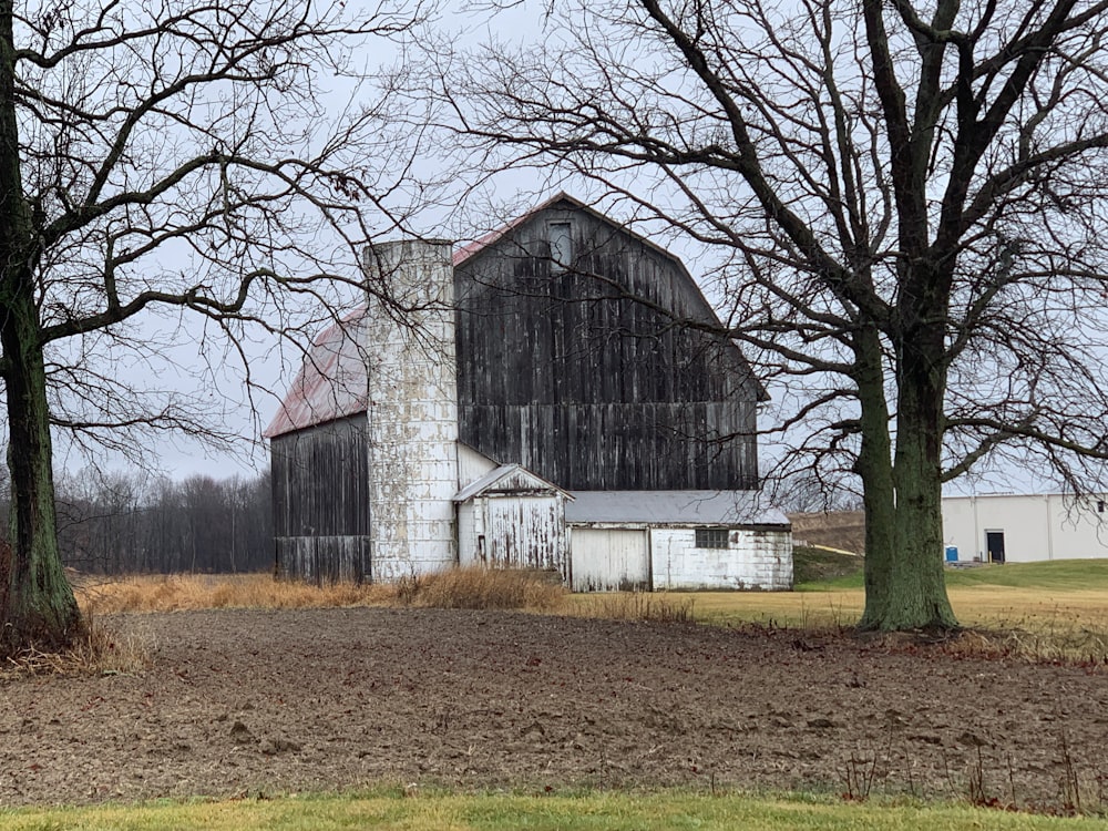 an old barn sits in a field next to some trees
