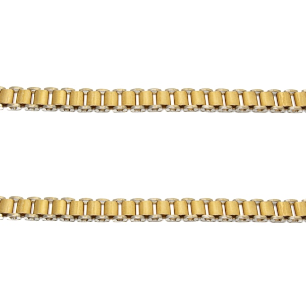 Two parallel gold chains are positioned horizontally against a plain white background. The links of the chains are cylindrical and interconnected evenly.