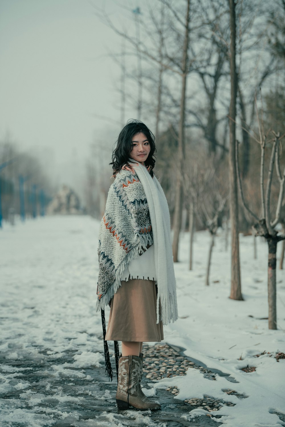 a woman standing in the snow wearing boots and a scarf