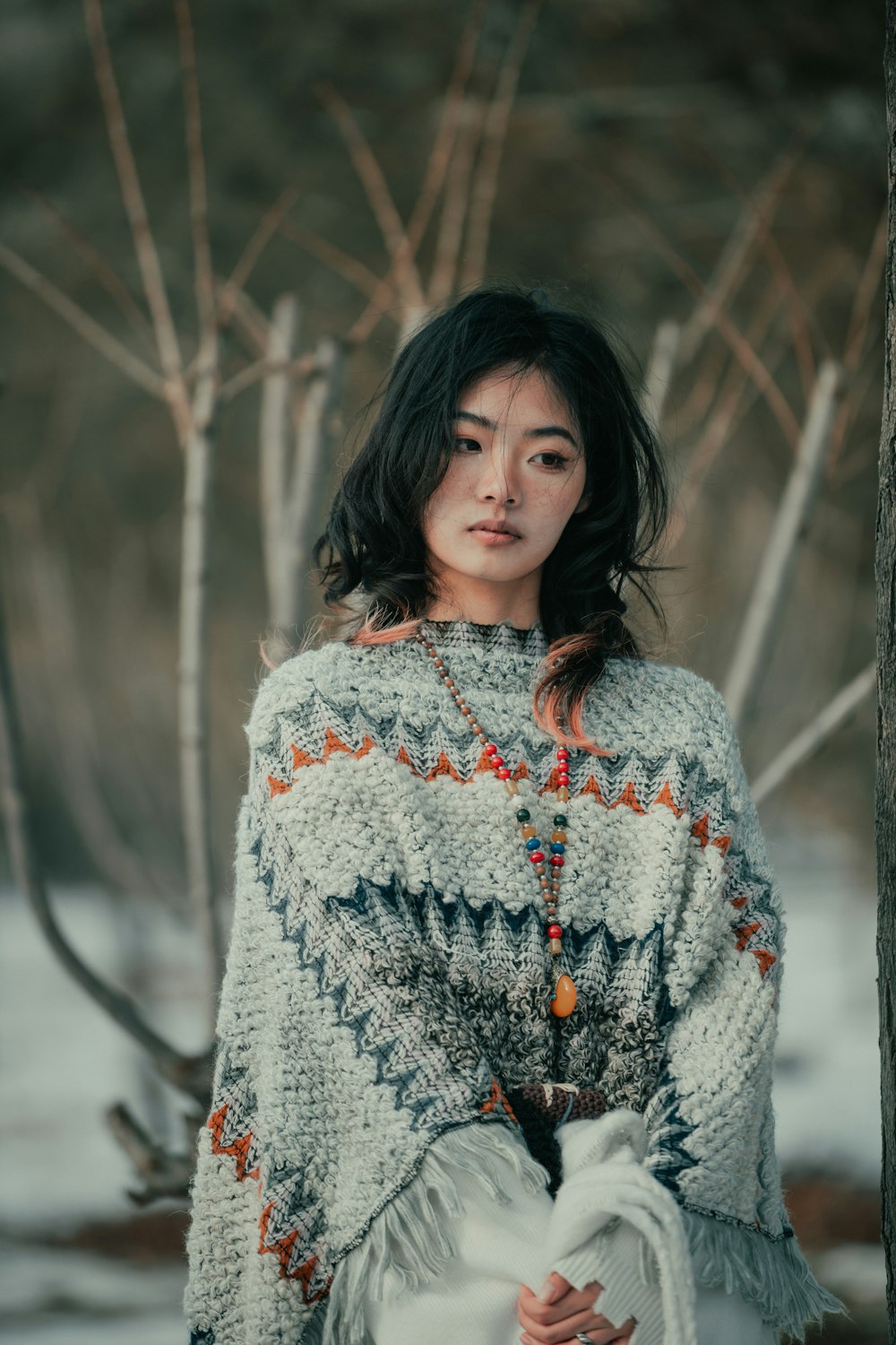 a woman in a sweater standing next to a tree