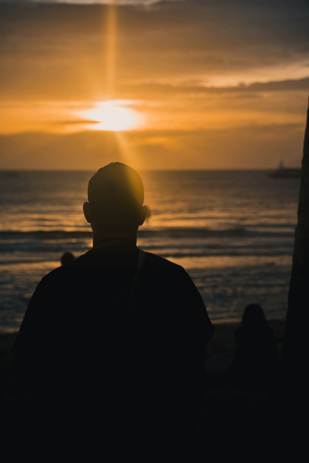 a man sitting in front of the ocean watching the sun go down
