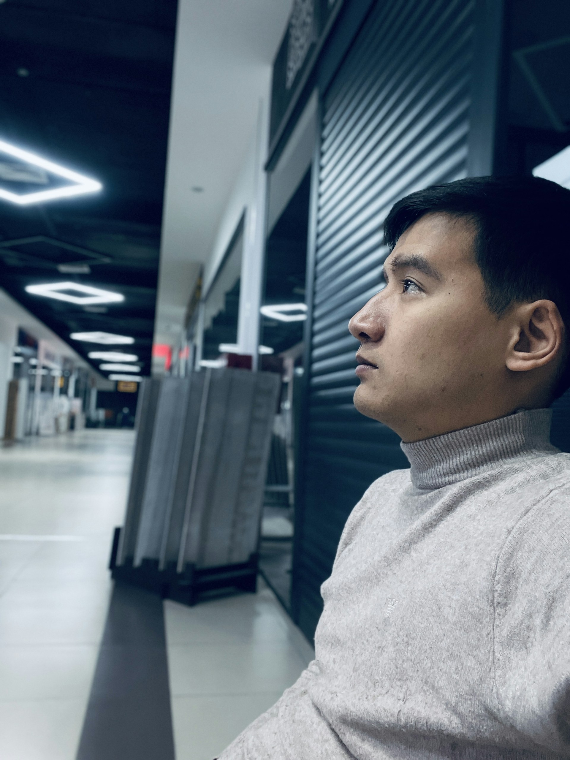 A close-up of a man wearing a soft gray sweater and minimalist watch, seated at a trendy café with muted decor.