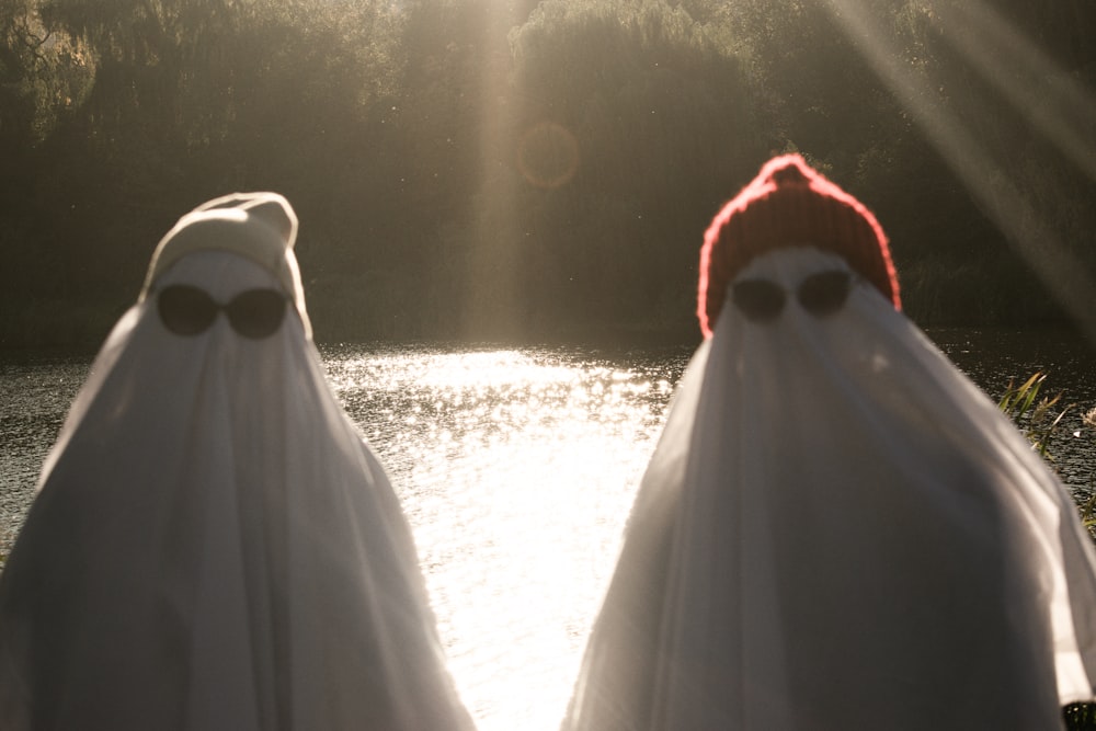 two people dressed in ghost costumes standing in front of a body of water