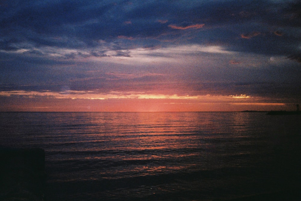 the sun is setting over the ocean on a cloudy day