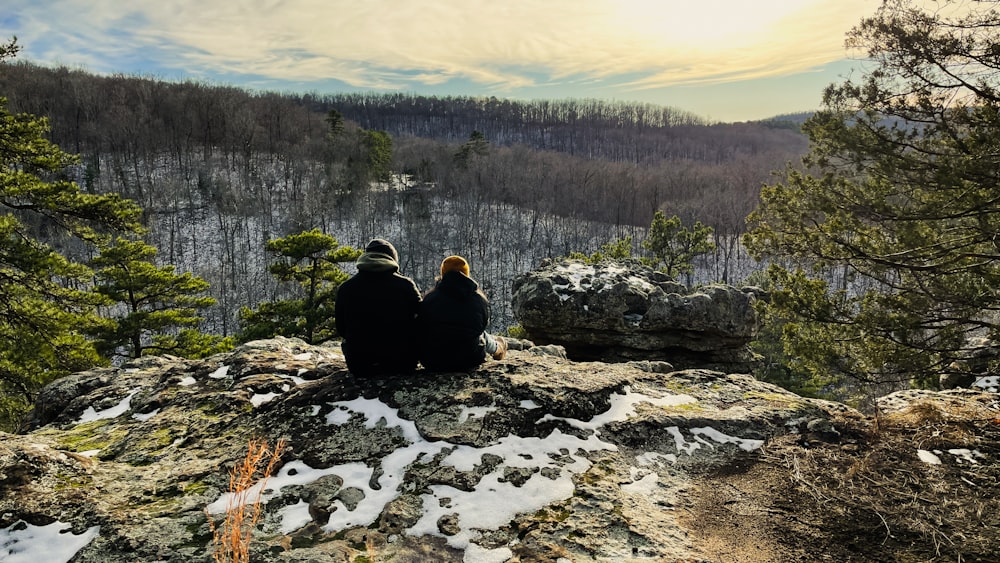 two people sitting on top of a rocky cliff