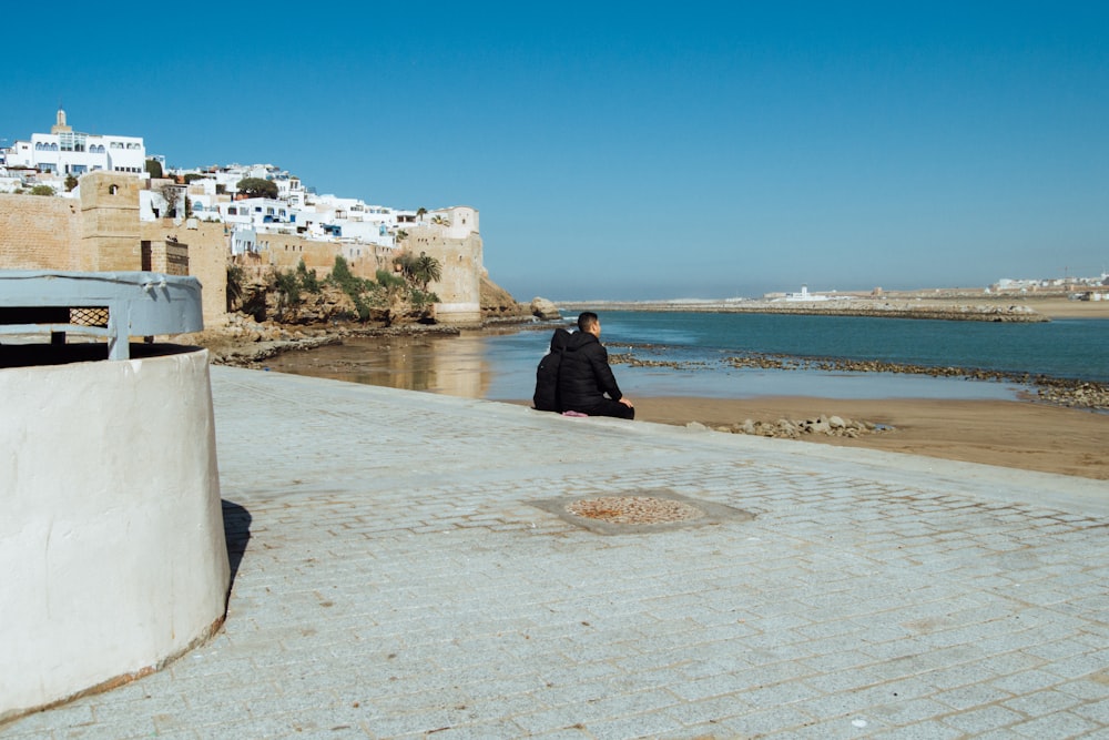 a man sitting on a wall next to a body of water