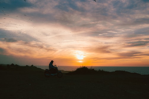 Sunset over a coastal highway with a motorcycle cruising along the edge