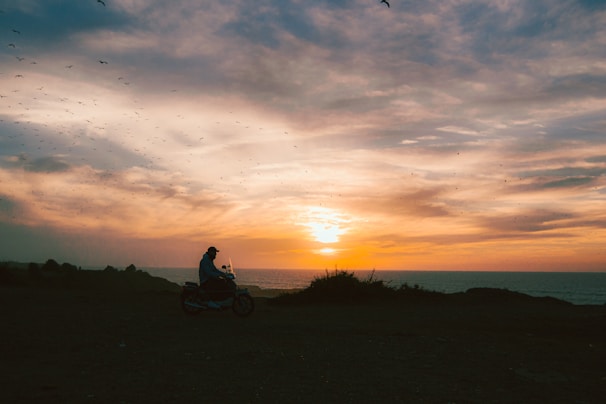 A dynamic shot of a motorcycle speeding along a coastal road at sunset, capturing motion and vibrant colors.