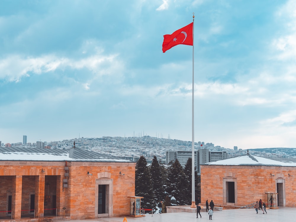 a red flag on top of a pole in front of a building