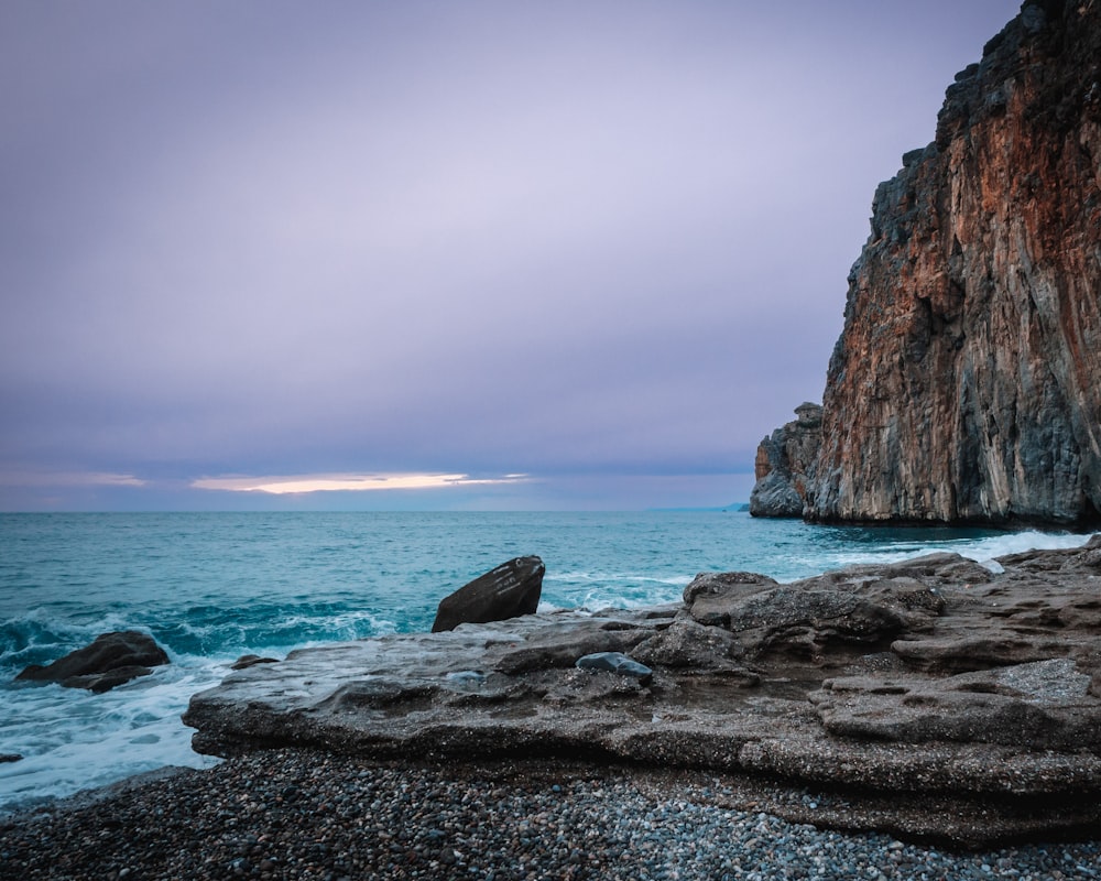 a rocky beach next to the ocean under a cloudy sky