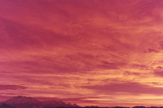 A vibrant sunset over a mountain range, casting warm orange and purple hues across the sky.