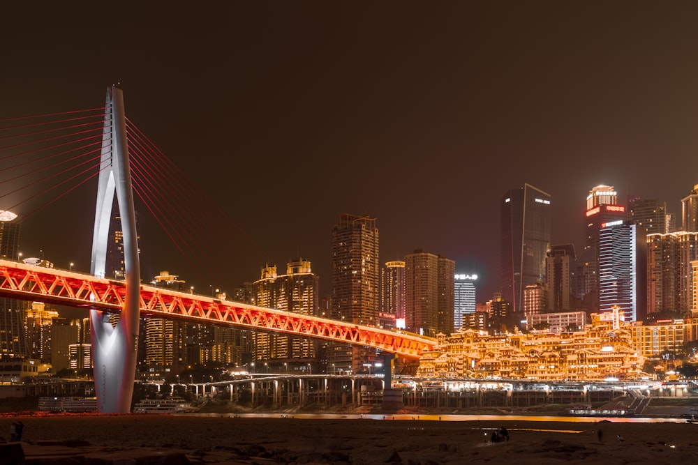 a red bridge over a body of water with a city in the background