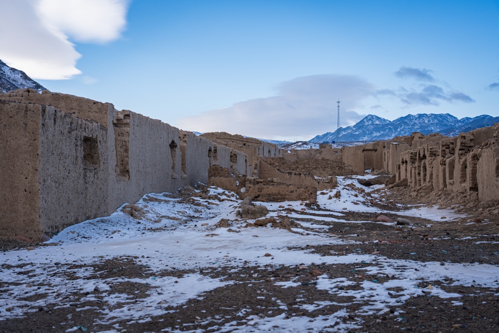 a dirt road with snow on the ground and mountains in the background