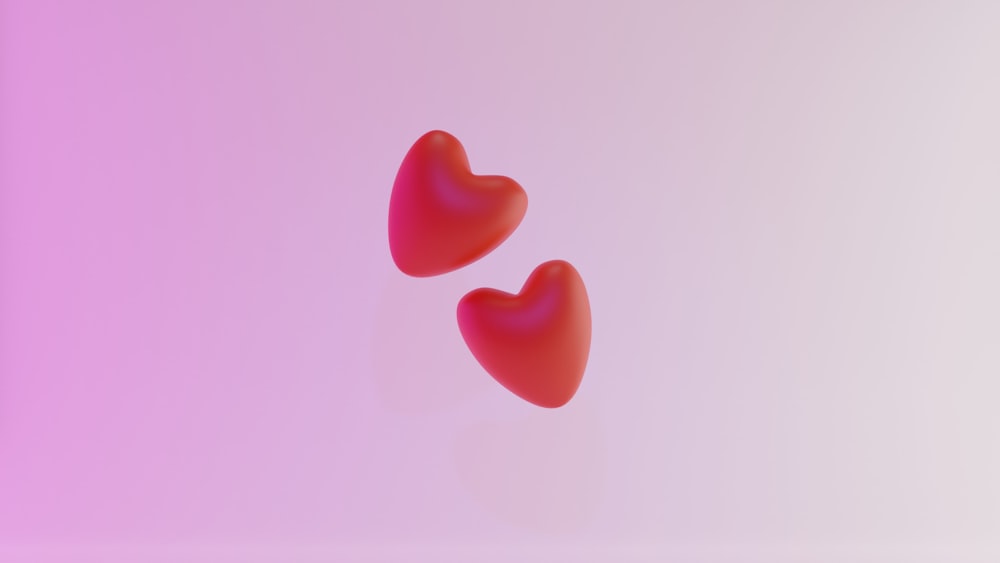 two red hearts floating in the air on a pink background