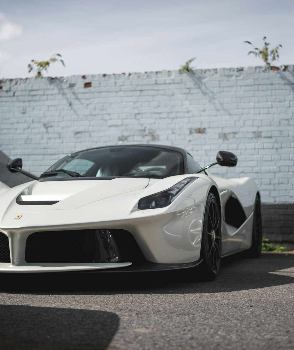 a white sports car parked in front of a white brick wall