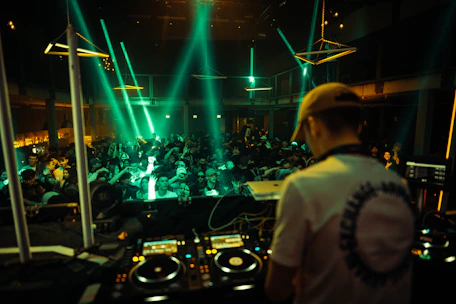 DJ mixing music at a lively party with colorful lights and happy guests dancing.