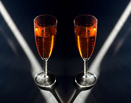 Elegant crowd in dark luxury setting, champagne glasses catching soft light without revealing faces.