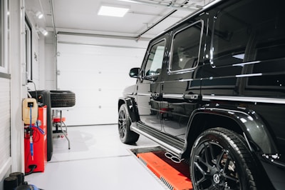 A sleek black SUV is parked inside a well-lit clean garage. To the left, there are multiple tools, a power outlet, and a set of spare tires. The garage door is closed, and the floor is spotless.