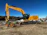 A heavy excavator carefully leveling a large construction site under a clear blue sky.