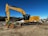 A hydraulic excavator digging soil on a large construction site under a clear blue sky.