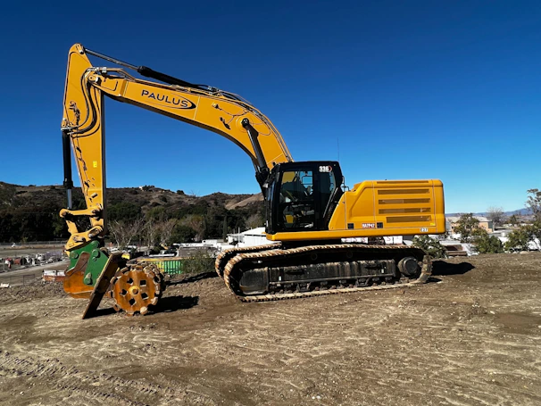 A powerful yellow excavator digging on a construction site under a clear blue sky.