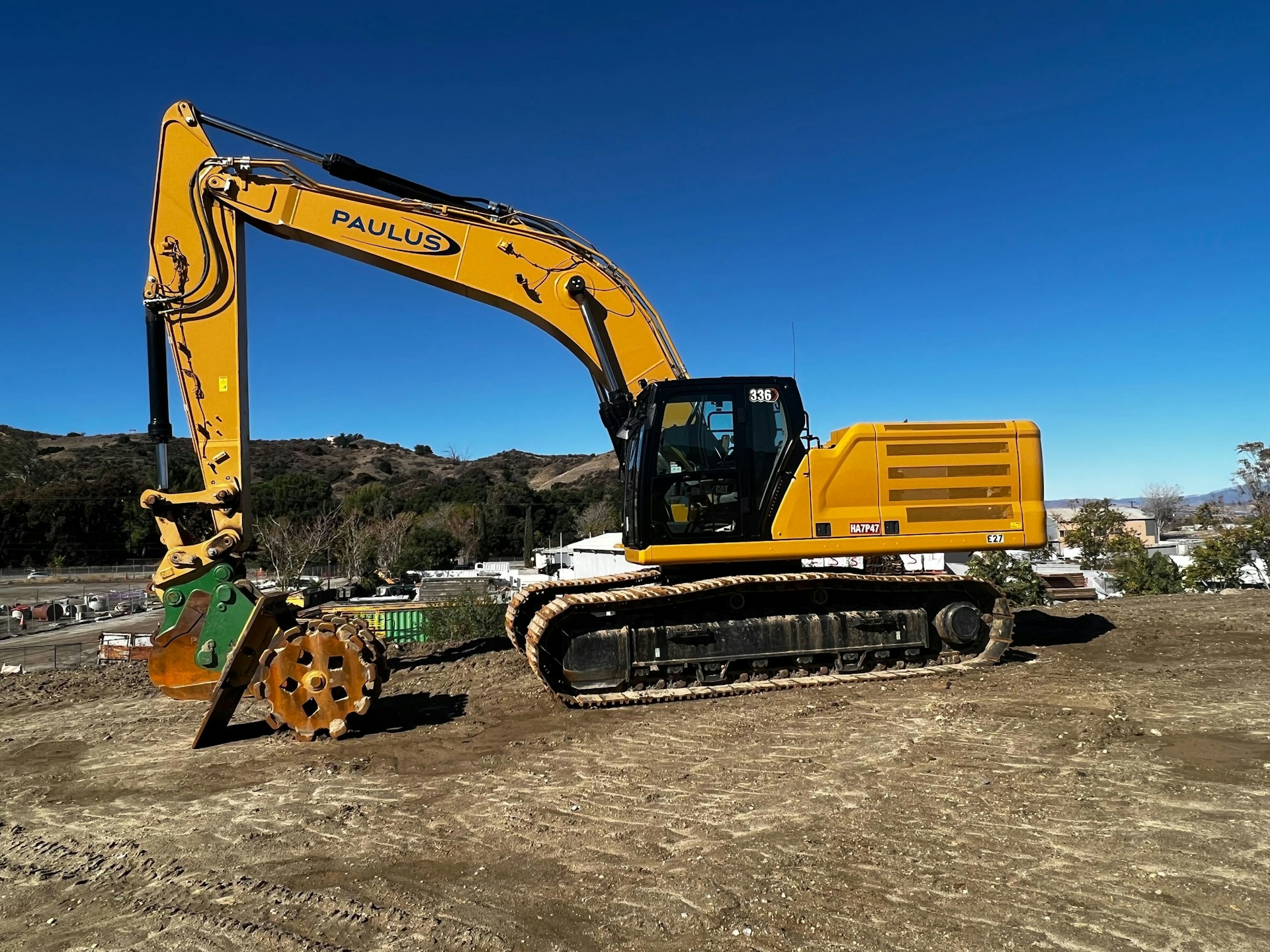 A powerful yellow excavator digging at a large construction site under a clear blue sky.