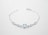 A delicate silver bracelet featuring a central heart-shaped blue gemstone flanked by two smaller round white stones on each side, all linked with a fine chain.