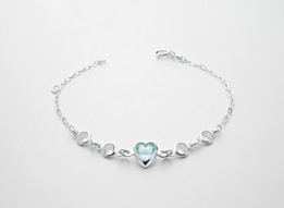 A delicate silver bracelet featuring a central heart-shaped blue gemstone flanked by two smaller round white stones on each side, all linked with a fine chain.