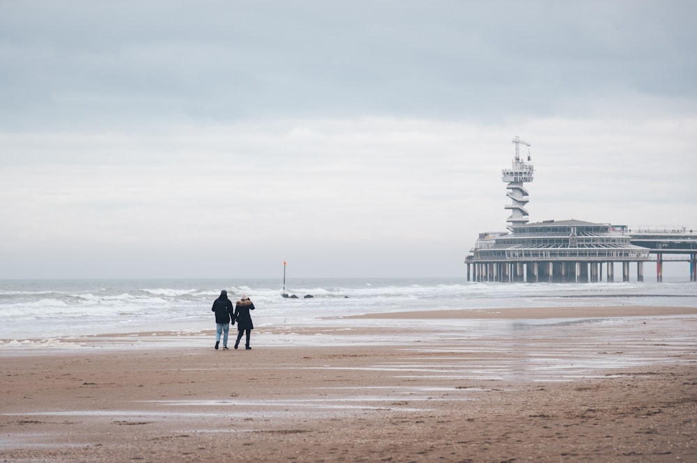 a couple of people standing on top of a sandy beach