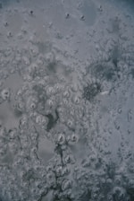 Patterns of bubbles trapped in ice are visible, featuring intricate, swirling designs. The surface appears cold and smooth, with varying shades of gray and subtle hints of green.