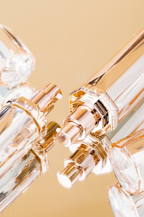 A close-up of elegant perfume bottles with gold and clear glass design. The bottles are artistically arranged against a reflective gold background, emphasizing their luxurious and sophisticated appearance.