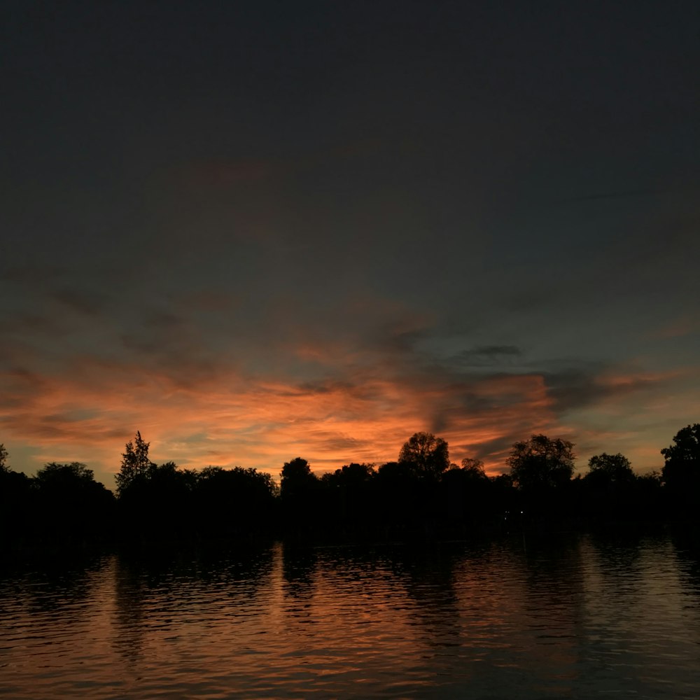 a sunset over a body of water with trees in the background