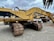 Several large yellow excavators with 'CAT' branding are parked on a gravel surface under a cloudy sky. The machines feature large metallic tracks and articulated arms, typically used for heavy-duty digging and construction work.