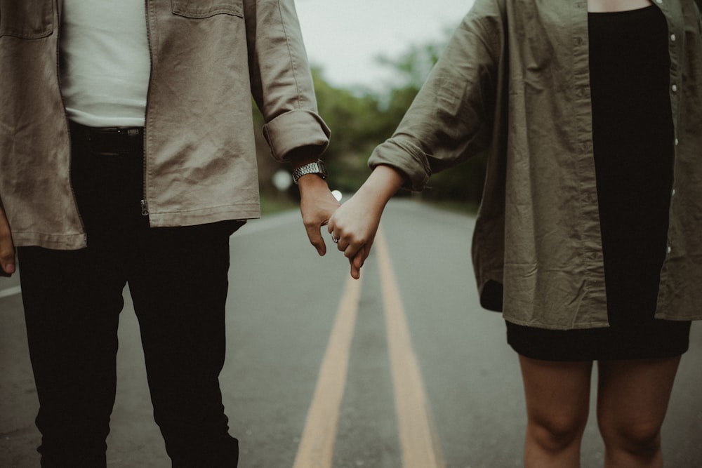 a couple holding hands while walking down a road