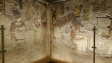 Ancient Egyptian wall carvings depict figures in regal attire, featuring pharaohs and deities. Hieroglyphics are inscribed above and around the figures, adding to the historical richness. The artwork demonstrates intricate detailing and craftsmanship typical of ancient Egyptian art.