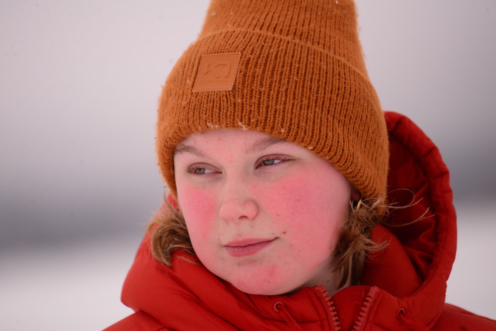 a young girl wearing a red coat and a brown hat