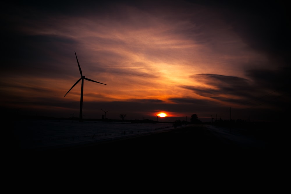 the sun is setting behind a wind turbine