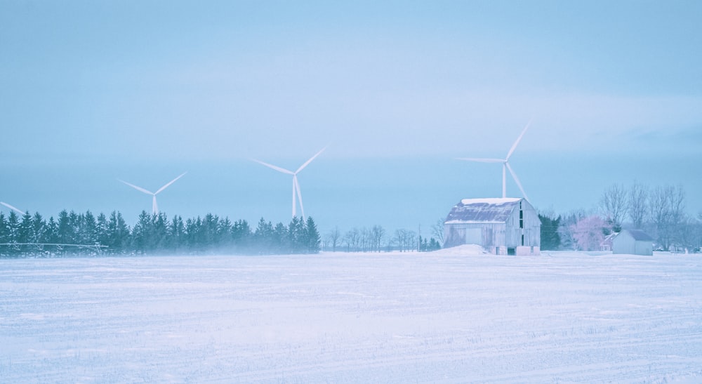 a snow covered field with a barn and windmills in the background